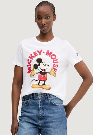 T-shirt en coton blanc avec un grand graphique coloré de Mickey Mouse. Texte "MICKEY MOUSE" en rouge en arc au-dessus du graphique. Coupe décontractée.