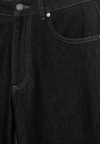 Fekete farmernadrág klasszikus, ötpocketes kivitelben, kontrasztos fehér varrással és ezüst színű gombbal a rögzítéshez.