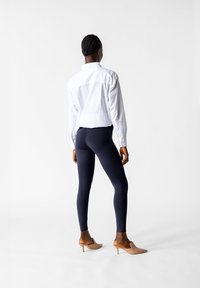 Biała koszula z guzikami, granatowe legginsy i beżowe klapki na obcasie. Legginsy są dopasowane, a koszula ma długie rękawy i klasyczny kołnierzyk.