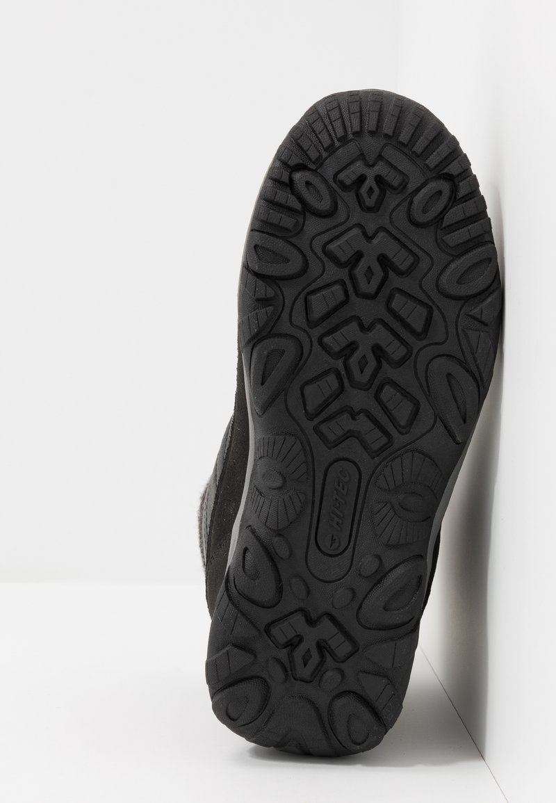 Suela de zapato de senderismo negro con un patrón de tracción de goma texturizada, presentando un logo y ranuras definidas para agarre y estabilidad.