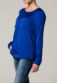 Blå långärmad blus i mjukt tyg, med knappstängning fram, bröstficka och avslappnad passform. Kombineras med ljusa denimjeans.