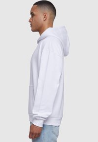 Witte hoodie met een kangoeroezak, een trekkoordkap en geribde manchetten. Heeft een comfortabele pasvorm en een zachte textuur. Gedirigeerd met lichtblauwe jeans.