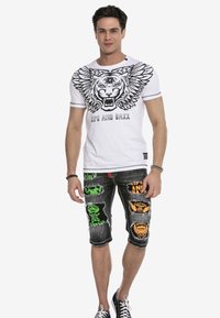 Weißes Baumwoll-T-Shirt mit einem schwarzen Tigerdesign und Flügeln. Schwarze Jeansshorts mit bunten Patches, ausgefransten Säumen und schmaler Passform.
