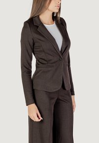 Hnedý herringbone blazer s priliehavým strihom, jedným gombíkom a klopovými revermi, v kombinácii s zodpovedajúcimi nohavicami.