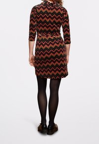 Svart och röd klänning med chevron-mönster, trekvartsärmar, krage, cinchad midja och utsvängd fåll, kombinerad med svarta strumpbyxor och skor.