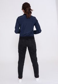 Giacca bomber blu navy con polsini e orlo elasticizzati neri, caratterizzata da una texture liscia e lucida e da un design aderente. Indossata con jeans neri a vita alta.