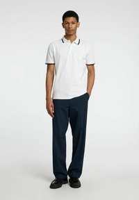 Chemise polo blanche avec des bordures noires, associée à un pantalon bleu marine foncé. Conçue avec des manches courtes et un col standard. Couleur unie.