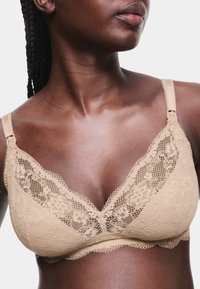 Sujetar beige de encaje con diseño de escote en V, patrones florales y tirantes ajustables. Textura suave con bordes delicados en forma de ondas.