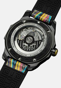 Schwarze automatische Uhr mit transparentem Gehäuseboden, ausgestattet mit bunten Streifenakzenten auf einem strukturierten schwarzen Gummiband. Wasserdicht bis 100 m.