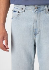 Lys blå denimjeans med rett ben-design, som har en frontlomme, knappelukking og subtile slitninger på stoffet.