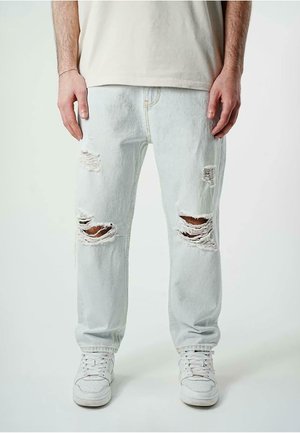 Light blue ripped jeans with large holes at the knees, made of denim, paired with white sneakers. Simple design and straight leg fit.