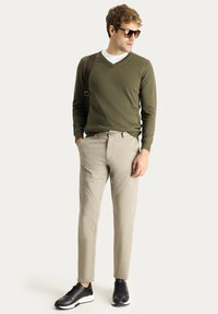 Suéter ligero en verde oliva con cuello en V, pantalones beige ajustados y zapatillas negras. Los complementos incluyen gafas de sol grandes y un bolso de hombro marrón.