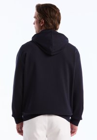 Sweat à capuche navy avec une texture lisse, des poignets côtelés et un ourlet droit, présentant un design minimaliste et une capuche fonctionnelle.