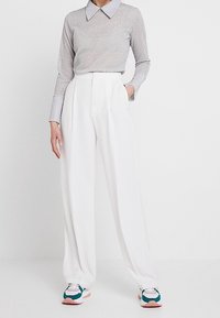 Haut gris clair à manches longues avec un grand col ; pantalon blanc plissé ; baskets sportives avec des touches de bleu sarcelle, rose et blanc.