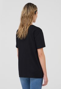 T-shirt in cotone nero con una vestibilità rilassata, maniche corte e scollatura a girocollo, caratterizzato da un design semplice e senza grafiche o motivi visibili.