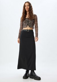 Leopardenmuster Crop-Top mit langen Ärmeln und ausgeschnittenem Vorderteil, kombiniert mit einem langen, enganliegenden schwarzen Rock und klobigen schwarzen Stiefeletten.
