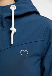 Sudadera azul marino con cordones blancos y bordado de un pequeño corazón en el bolsillo del pecho. Textura suave y detalle de costuras visibles.