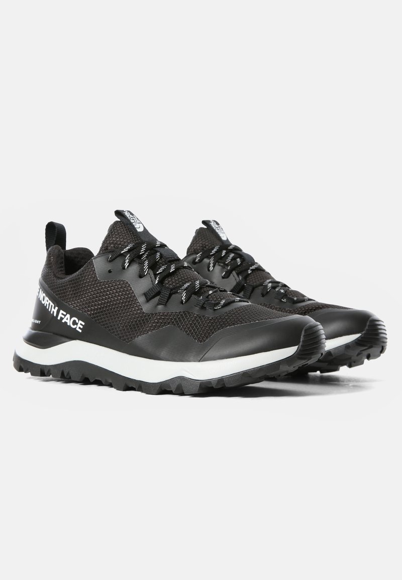 Chaussures de sport noires avec une tige en mesh texturé, une semelle intermédiaire blanche contrastante, un bout renforcé et des lacets noirs, conçues pour la performance en extérieur.