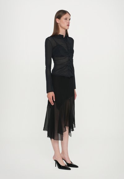 Black sheer blouse with long sleeves, button front, and gathered detailing paired with a black asymmetrical skirt and black pointed-toe heels.