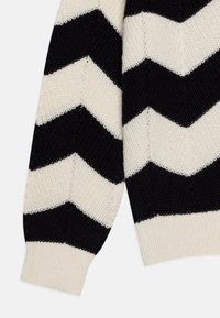 Pull en tricot avec un motif en chevron noir et beige, présentant un col et des poignets côtelés. Le matériau a une finition texturée.