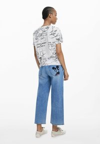 Tricou alb cu schițe negre ale lui Mickey Mouse; blugi evazați albastri cu un patch al lui Mickey Mouse pe buzunarul din spate; material texturat; design casual.