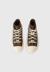 Brūni augstie čības ar baltām šņorēm un gumijas zole. Iezīmējas ar strukturētu virsotni un kontrastējošu balto purngalu. Oderēta iekšpuse.