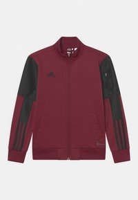 Vínová sportovní bunda s černými doplňky, zapínáním na zip, žebrovanými manžetami a třemi černými pruhy na rukávech. Má přední kapsy a logo.