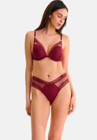 Ensemble de lingerie bordeaux avec un soutien-gorge lisse orné de dentelle et de bretelles ajustables, associé à une culotte taille haute assortie et des accents transparents.