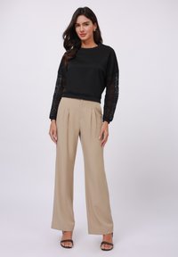 Zwarte top met lange mouwen en kantdetails op de mouwen, gecombineerd met beige high-waisted wijde broek en zwarte open teen hakken.