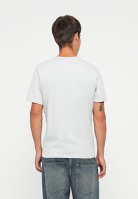 Camiseta de manga corta color gris claro con cuello redondo, textura suave y corte relajado. Llevada con jeans de mezclilla grises que tienen bolsillos traseros.