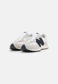 Chaussures de sport beige et blanches avec une tige en daim et en maille, présentant une bande d'accent noire et une semelle en caoutchouc texturé.