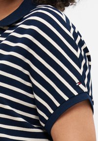 Polo a righe blu navy e bianche con colletto, dotato di maniche corte e un piccolo accentuato con marchio sulla manica. Materiale in cotone.