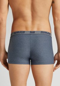 Šedé boxerky s texturovanou tkaninou, s tmavým páskem s brandingem "IUMAN". Design je přiléhavý, zobrazuje zadní pohled.