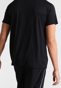 Tmavě šedé atletické tričko s volným střihem, krátkými rukávy a hladkou texturou. Má jemné švy podél ramenních švů.