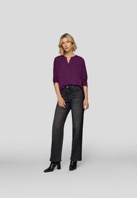 Lila Bluse mit langen Ärmeln und zwei Brusttaschen, kombiniert mit hoch taillierten dunklen Jeans und schwarzen Stiefeletten mit Absatz.