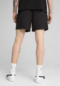 Shorts noirs en tissu léger, au design décontracté, avec des coutures visibles et des poches latérales, associés à des baskets blanches.