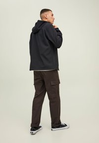 Chaqueta negra con capucha, de tela suave, camiseta gris debajo, pantalones cargo marrones con bolsillos laterales y zapatillas negras con suelas blancas.