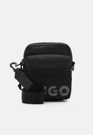Zwarte crossbodytas met een gestructureerd mesh front en ritssluiting. Voorzien van een afneembare band met geperst merklogo. Compacte en rechthoekige vorm.