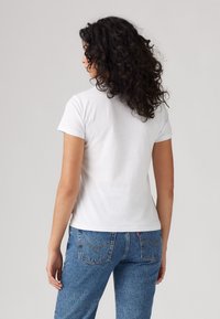 Witte katoenen t-shirt met korte mouwen, aansluitende stijl, gladde textuur, gecombineerd met blauwe denim jeans met stiksels op de achterzak.
