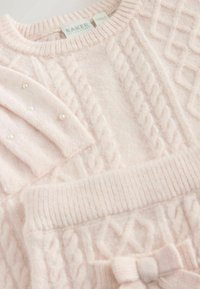 Gaiši rozā adīta jaka ar kabeli, ribotām apkaklītēm un malām, ar dekoratīvām pērlītēm uz vienas piedurknes un izsistās lenti.