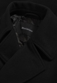 Čierny vlnený kabát s výstrihom v tvare klopy, označený "Matinique," s hladkou vnútornou podšívkou a jemným detailom vreciek.