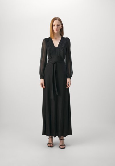Robe maxi noire avec de longues manches transparentes, un décolleté en V profond, un corsage volé et une ceinture à la taille. Tissu lisse avec un design longueur cheville.