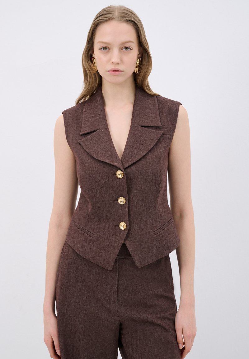 Bruine, mouwloze vest met een gekarteld kraag, vijf gouden knopen en zijzakken. Textiel met textuur in een op maat gemaakte pasvorm.