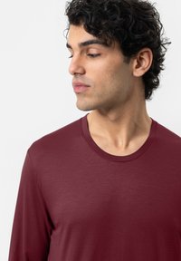 Langarmshirt in tiefburgunder, aus weichem Material mit Rundhalsausschnitt und glatter Textur, mit minimalen Nähdetails.