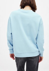 Sudadera de gran tamaño en azul claro con cuello redondo y mangas largas. Textura suave, puños y cinturilla acanalados. Vista trasera mostrada.