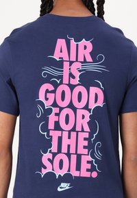 Tmavě modré bavlněné tričko s výrazným růžovým nápisem na zádech "AIR IS GOOD FOR THE SOLE", obklopeným světle modrými vlnitými detaily. Logo Nike.