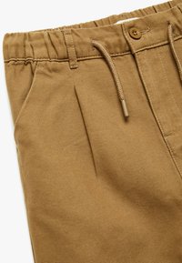 Brune bomuldsbukser med en tekstureret overflade, læg, elastisk talje og en snor med plastikhåndtag til justering.