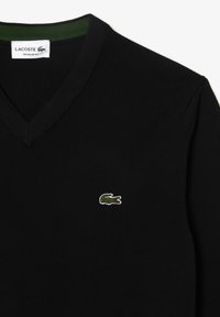 Maglione nero a scollo a V in tessuto lavorato a maglia, con un accento verde nel colletto e un piccolo logo di coccodrillo ricamato sul petto.