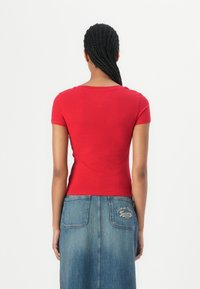 T-shirt rouge ajusté avec des manches courtes, en tissu doux, associé à une jupe en jean bleue avec des détails de logo brodés à l'arrière.