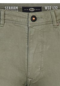 Pantalones verde oliva con cremallera, bolsillos frontales y cierre de botón. Presentan costuras dobles y una textura suave. Etiqueta de la marca visible.
